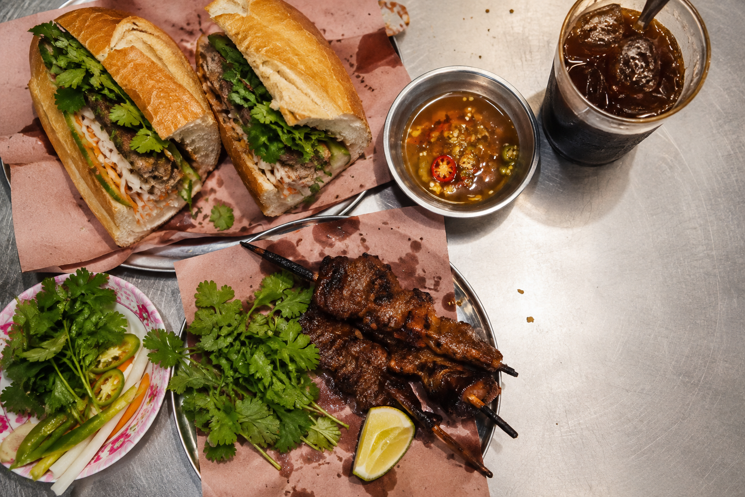 Bánh mì, grilled pork skewers, herbs and iced coffee on a steel table