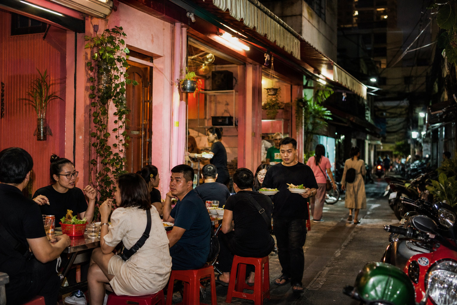 A busy pink street-food restaurant in a Saigon alley at night